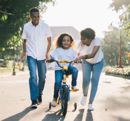 Parents teach a young African American girl how to ride a bike.