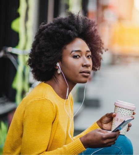 lack woman with a smartphone and coffee wearing headphones.