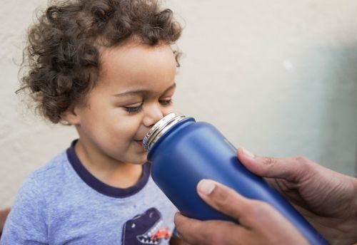 Padre ayuda a su hijo a beber de una botella de acero inoxidable.