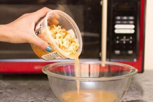 Young woman pours soup from a plastic container into a glass bowl so that she can microwave it safely. 